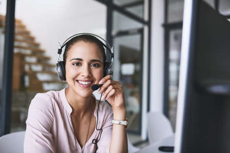 Good day how may I be of service. Portrait of a cheerful businesswoman talking to a customer using a headset while looking at the camera.の写真素材