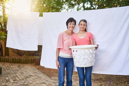 Shes helping mom with the chores. Portrait of a mother and daughter hanging up laundry together outside.の写真素材