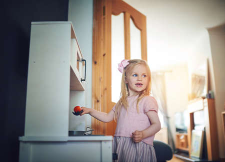 Dinners on me tonight. Shot of an adorable little girl playing with a toy kitchen set at home.の写真素材