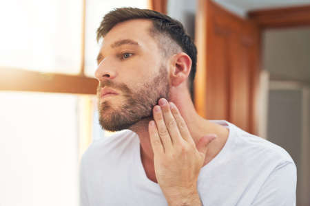 Maybe I should shave it all off. Shot of a handsome young man going through his morning routine at home.の写真素材