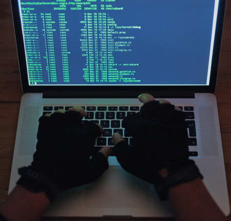 Your network has been breached. Shot of an unrecognisable hacker using a laptop in the dark.の写真素材