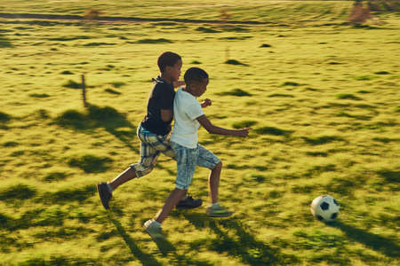 Football fun with a friend. Shot of a two children playing soccer together in a field outside.の写真素材