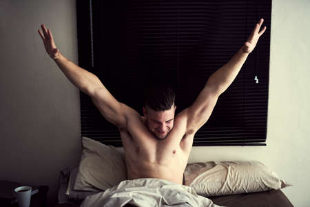 Today is going to be awesome. Shot of a handsome young man stretching after waking up rested in bed.の写真素材