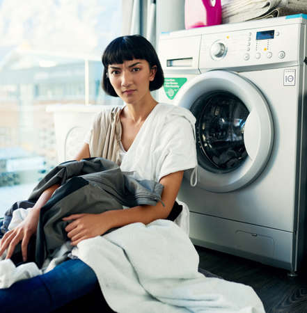 When do I get the day off. Shot of a young woman doing her laundry at home.の写真素材