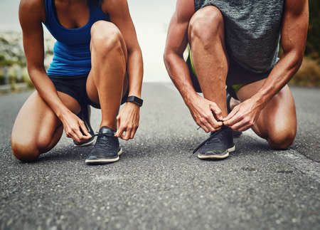 Tying our laces together. Shot of an unrecognizable couple training for a marathon outdoors.の写真素材