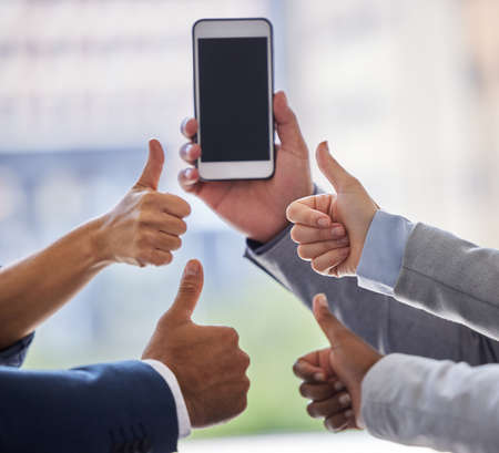 Weve got our million dollar idea right here. Cropped shot of an unrecognizable group of businesspeople standing with their thumbs up while a coworker holds a cellphone.の写真素材