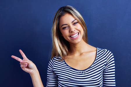 World peace. Portrait of a beautiful young woman giving a peace sign.の写真素材