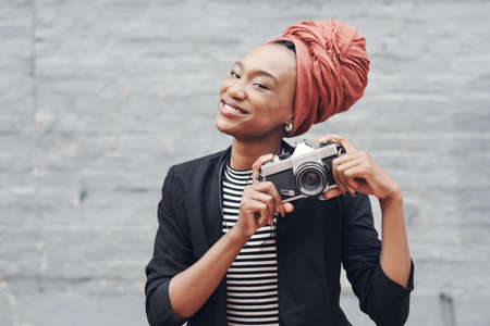 Photography is my favourite hobby. Cropped portrait of an attractive young businesswoman posing with her camera against a grey brick wall outside.の写真素材