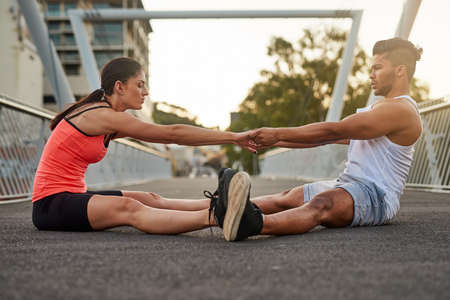 Lemme give you a hand. Shot of a young couple warming up on a bridge before their workout.の写真素材