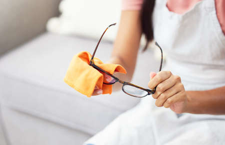 Theyre no good if theyre not clean. Cropped shot of a woman cleaning her glasses while sitting at home.の写真素材