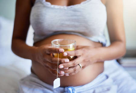 Some tea for me and my sweety. Cropped shot of a pregnant woman relaxing at home with a glass of tea.の写真素材