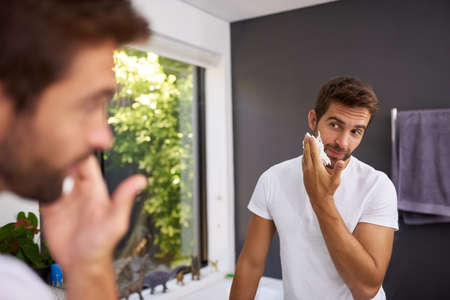 Shaving cream first to protect my skin. Cropped shot of a handsome man applying shaving cream on to his face in the bathroom at home.の写真素材
