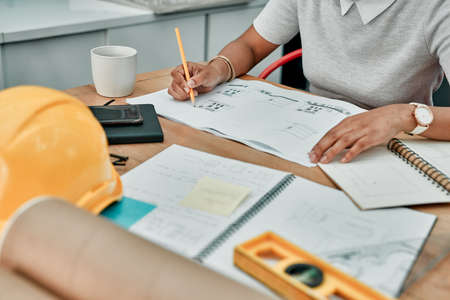 Putting her big plans into place. Closeup shot of an unrecognisable architect working with blueprints in an office.の写真素材