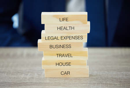 The more youre covered, the better youll feel. Shot of an unrecognisable businessman assembling wooden blocks with insurance related words on them.の写真素材