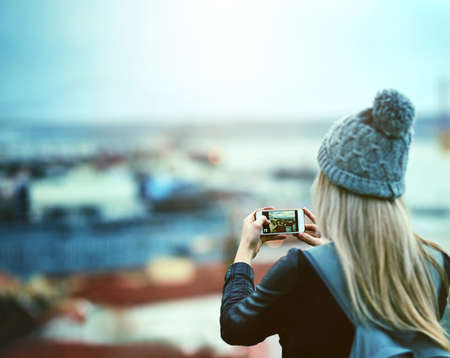 Shes a memory collector. Rearview shot of a young woman using a cellphone to take pictures of a city...