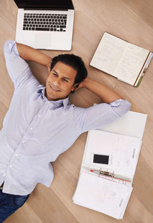 Taking a break from his work. High angle shot of a young businessman lying on his home floor surrounded by work.の写真素材
