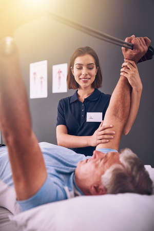 As far as you can. Cropped shot of a young female physiotherapist treating a mature male patient.の写真素材