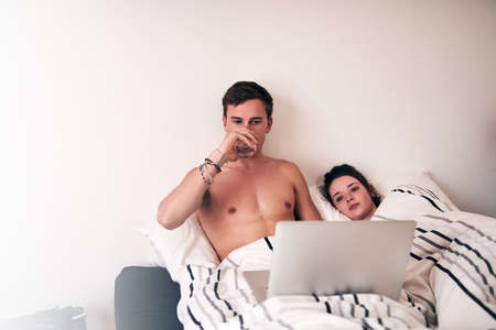 Hes got their weekend all planned out. Shot of a young couple using their laptop in bed.の写真素材