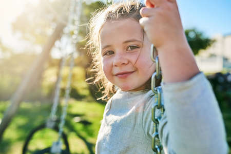 Summer is in full swing. Portrait of a cute little girl sitting on a swing in a park.の写真素材