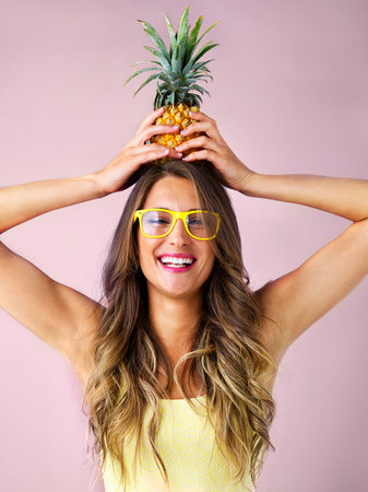 Be like a pineapple, always wear your crown. Studio shot of a young woman holding a pineapple against a pink background.の写真素材