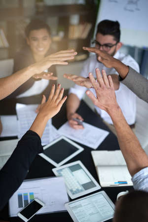 Succeeding is this teams top priority. Shot of a group of coworkers with their hands in a huddle while sitting together around a table in an office.の写真素材