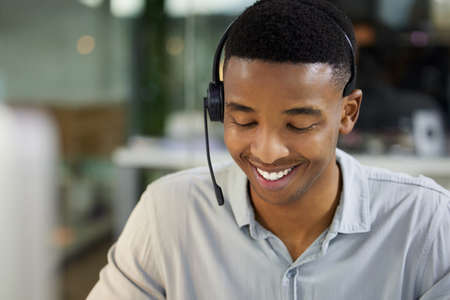 Great customer support is great business. Shot of a young man using a headset and computer in a modern office.の写真素材