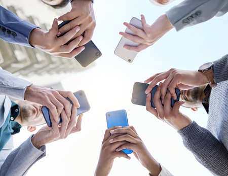 Connecting faster for the best way forward. Shot of a group of unrecognisable businesspeople using their cellphones together at and outside meeting.の写真素材