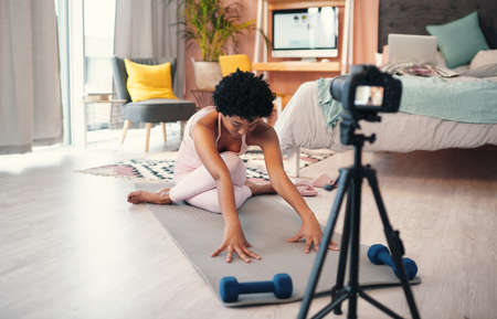 Filming a fitness tutorial for her followers. Shot of a young woman recording herself while exercising at home.の写真素材
