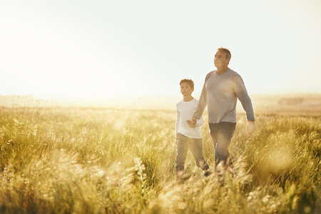 Showing him the beauty of nature. Shot of a man taking his son for a walk out on an open field.の写真素材