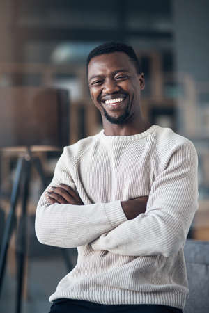 Welcome to my humble abode. Cropped shot of a handsome young man sitting alone in his living room with his arms folded.の写真素材