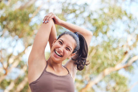 Good morning, time to stretch. Portrait of a sporty young woman stretching her arms while exercising outdoors.の写真素材