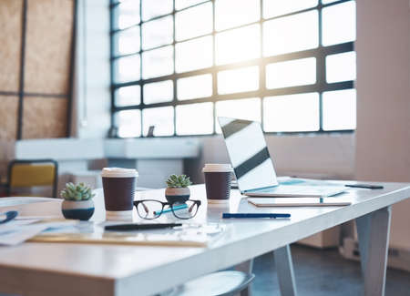 Ready for a new business day. Shot of a laptop, papers and coffee cups on an empty boardroom table in the office.の写真素材
