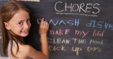 Noting some chores for the day. Portrait of a young girl marking chores off a chalkboard.の写真素材