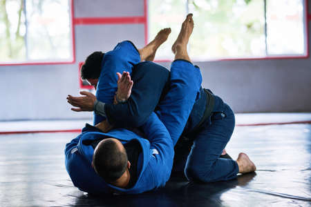 Almost all fights end up on the ground. Full length shot of two young male athletes sparring on the floor of their dojo.の写真素材