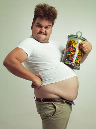 This will help me grow nice and big. Cropped shot of an overweight man holding a large jar of candy.の写真素材
