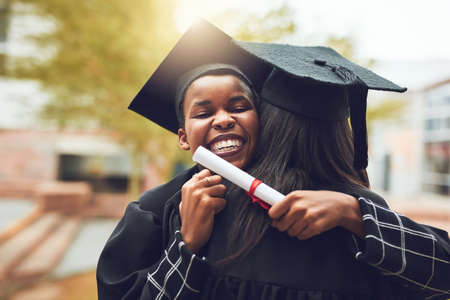 Our friendship got us through a lot of long nights. Shot of two graduates embracing each other on graduation day.の写真素材