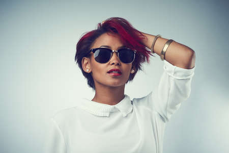 Just own your beauty. Shot of a beautiful young woman wearing sunglasses against a grey background.
