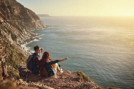 Take a look over there. High angle shot of an affectionate young couple taking in the view from a mountaintop.の写真素材