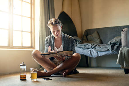 Nothing beats a good page-turner. Shot of a young man reading a book at home.の写真素材