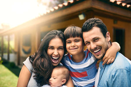 Our big happy family. Cropped portrait of a happy young family of four outside with their house in the background.の写真素材