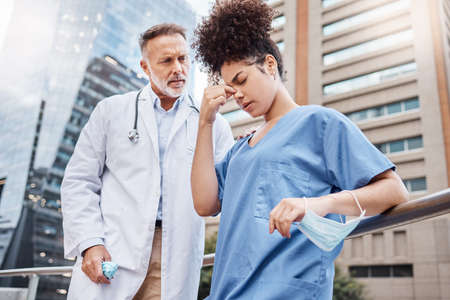 Long hours can take a toll when youve worked nonstop. Shot of a young female nurse suffering from a headache while talking to a colleague in the city.の写真素材