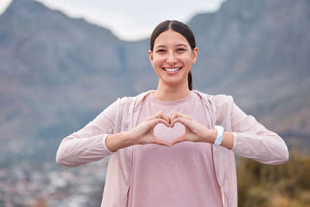 Taking care of her heart health. Shot of a young woman making a heart shape with her hands while exercising outdoors.の写真素材