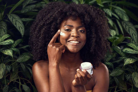 The less chemicals, the happier my skin. Shot of a beautiful young woman applying moisturiser to her face against a leafy background.の写真素材