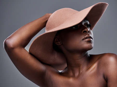We all glow differently. Shot of a beautiful young woman wearing a hat while posing against a brown background.の写真素材
