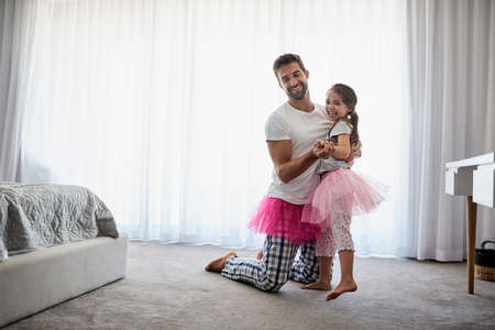 Leading her on a merry little dance. Full length shot of a handsome young man and his daughter dancing at home.の写真素材