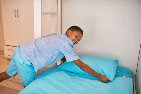Neatening the bed. Portrait of a young boy making up a bed.の写真素材
