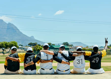 First baseball, then peace. Rearview shot of a team of unrecognizable baseball players embracing each other while sitting near a baseball field during the day.の写真素材