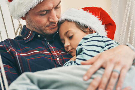 The safest spot in the whole wide world. Shot of an adorable little boy having a nap with his father in a hammock at Christmas.の写真素材