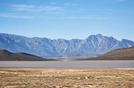 Where has the rain gone. Shot of a desolate landscape during the day with a small dried out dam in the middle.の写真素材