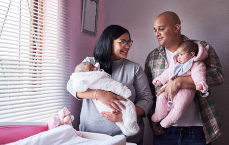 A home can never have too much love in it. Shot of a young man and woman carrying their twin baby girls at home.の写真素材